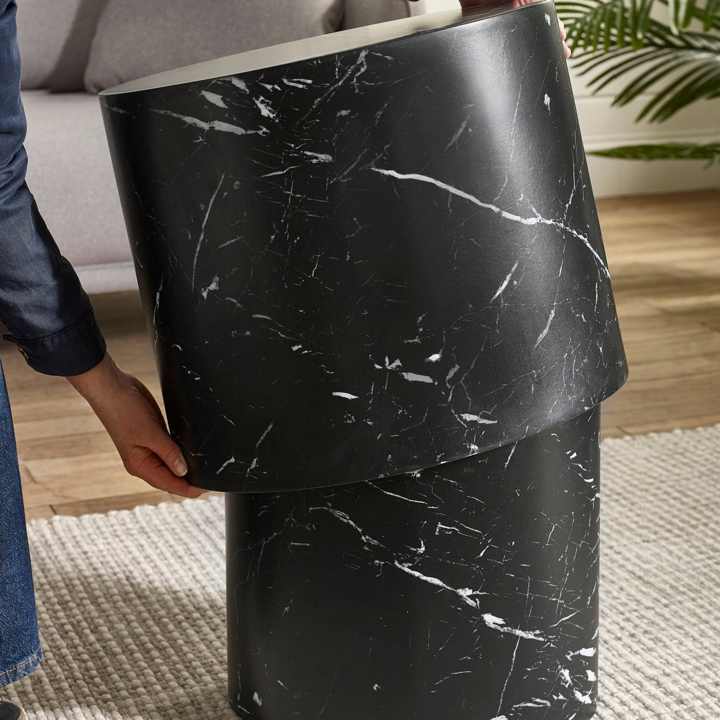 Hand lifting smaller oval black table with white marble veins stacked on larger matching table