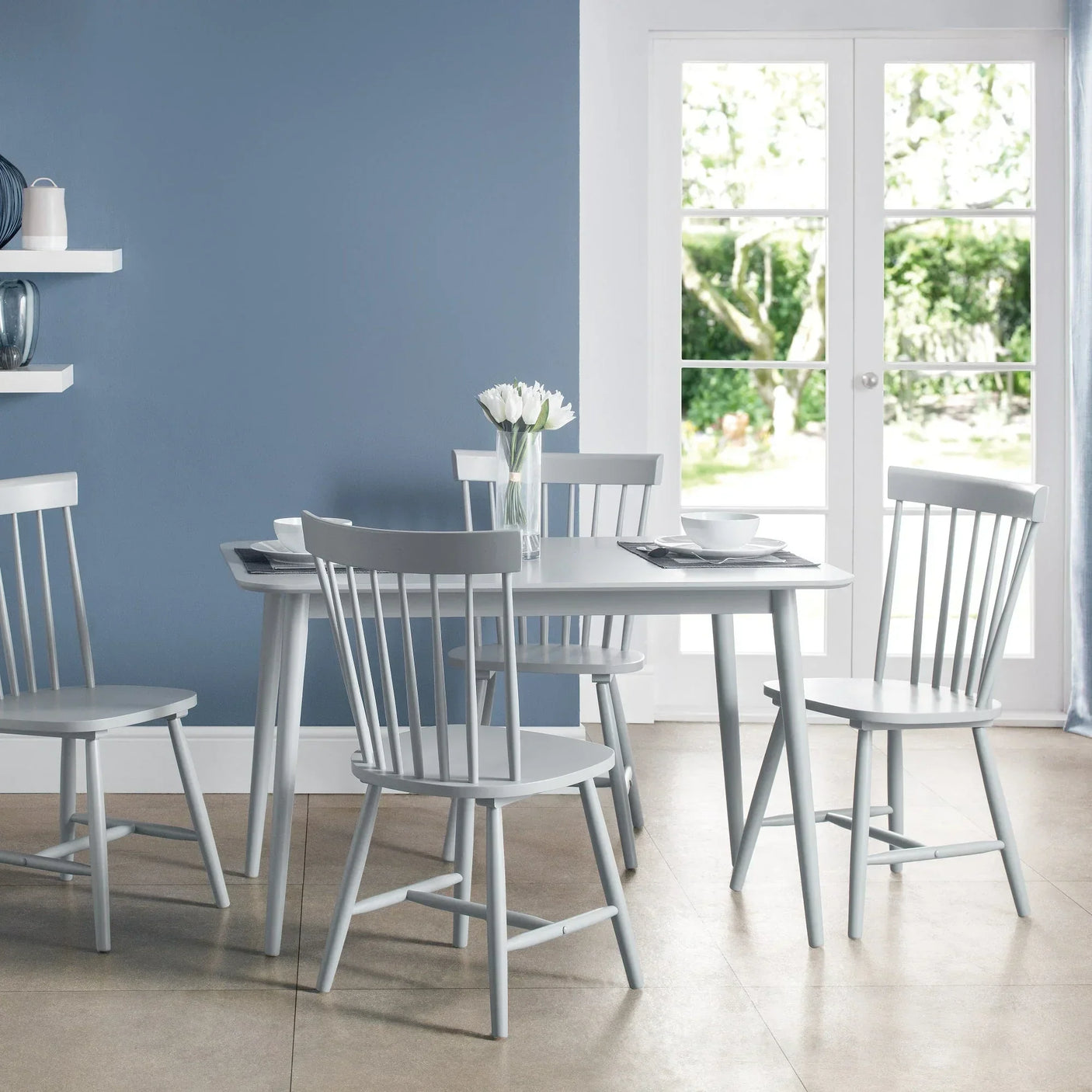 Grey dining table set with four matching chairs in a modern room with blue wall and tulips