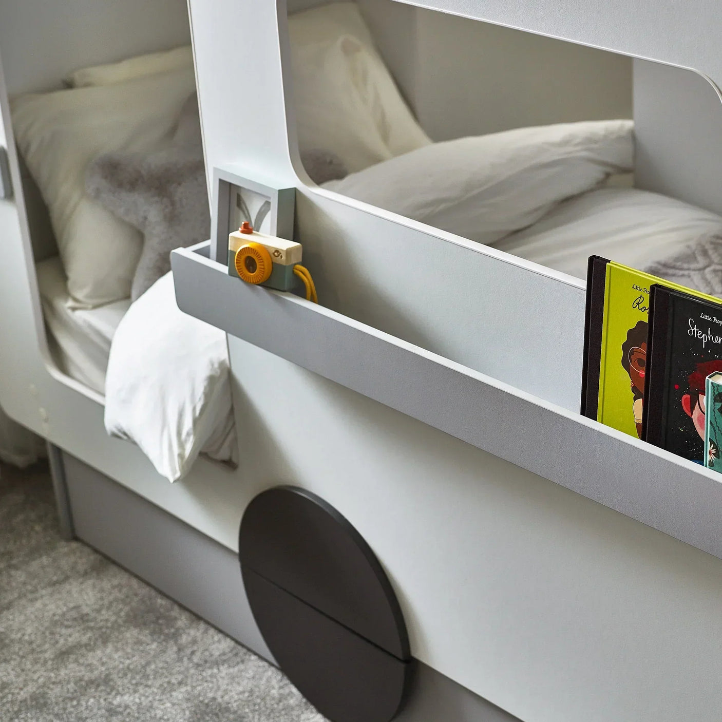 Tourer caravan bed with grey bedding, side shelf holding books and wooden toy camera
