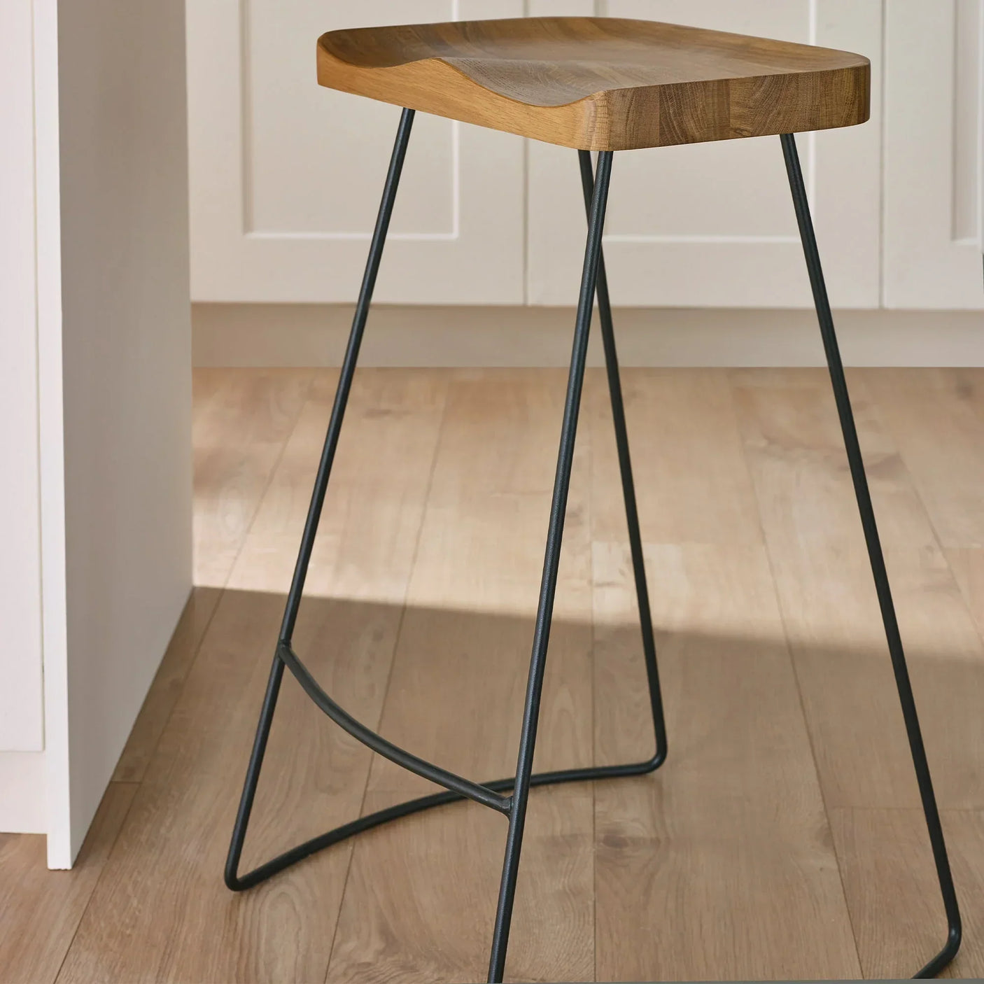 Solid oak bar stool with contoured seat and black metal legs on wooden floor