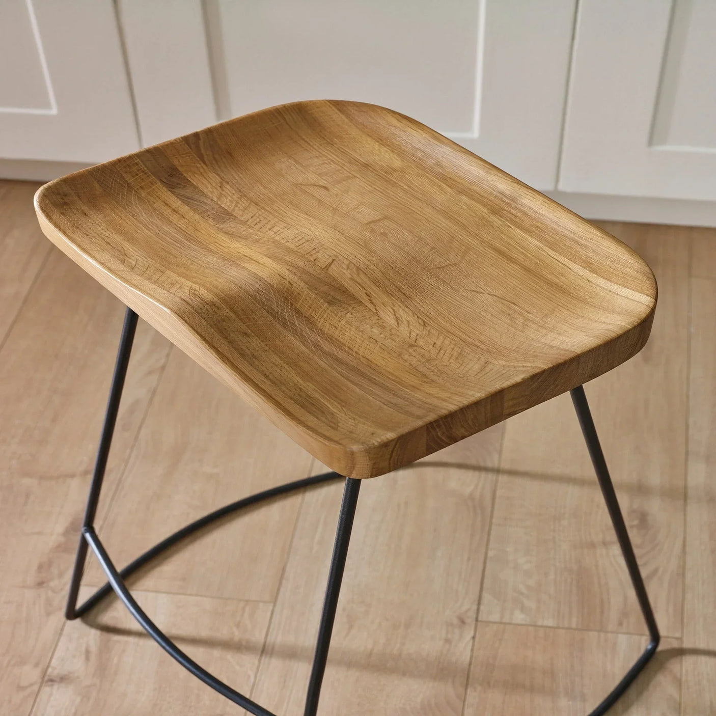 Solid oak bar stool seat with curved edges and black metal legs on wooden floor