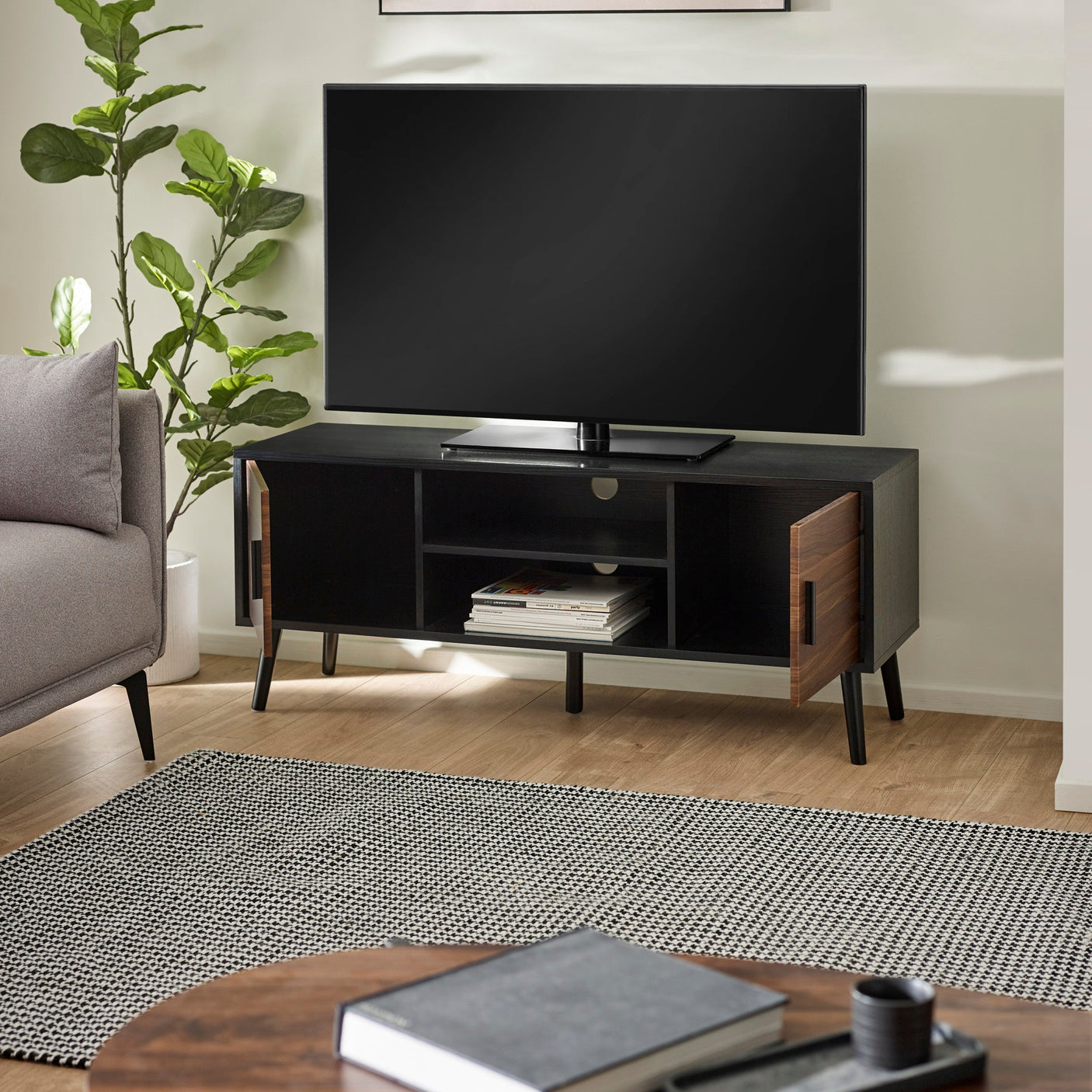Large TV unit with black wood frame and walnut doors ajar, showing empty shelves beneath a TV.