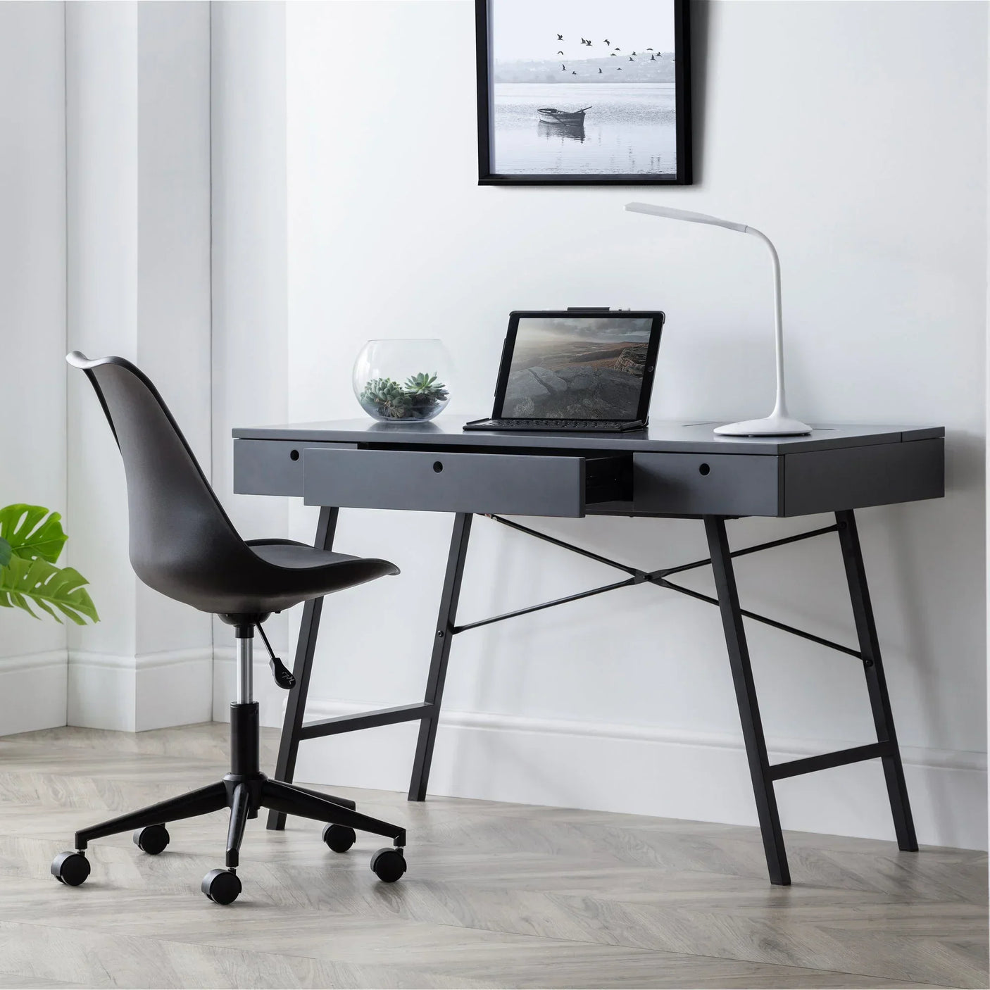 Grey desk with storage drawers, black office chair, laptop and lamp in modern home office