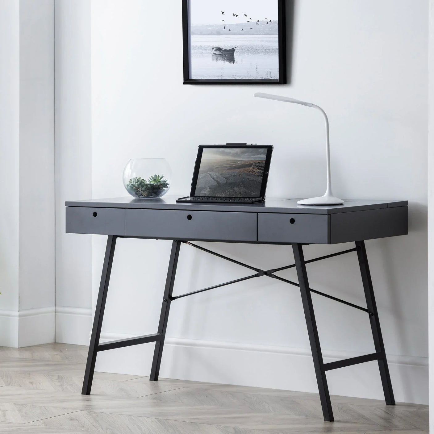 Grey desk with metal legs, three drawers, laptop, lamp, and glass bowl in modern room