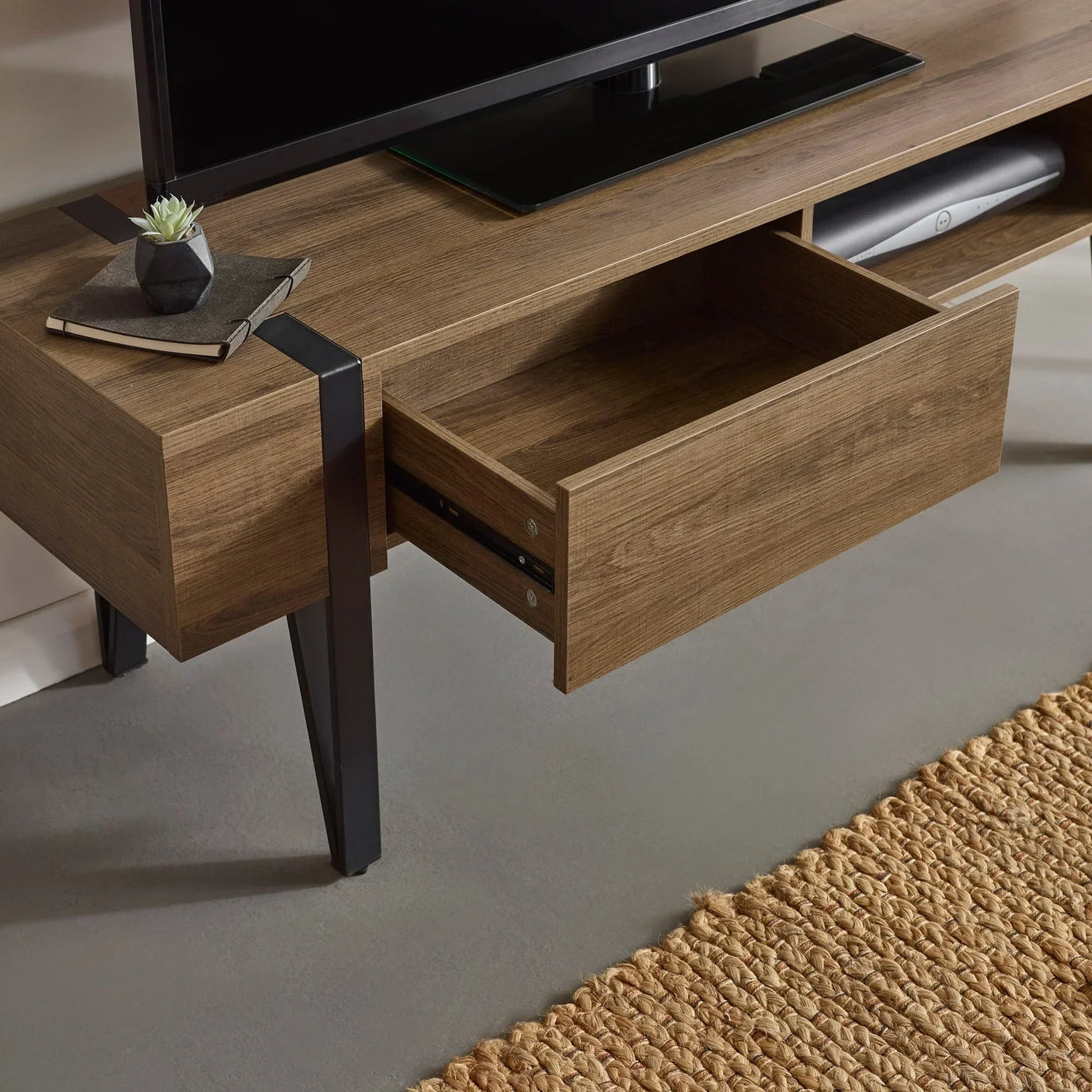 Wooden TV unit with open storage drawer, black metal legs, and tabletop accessories visible