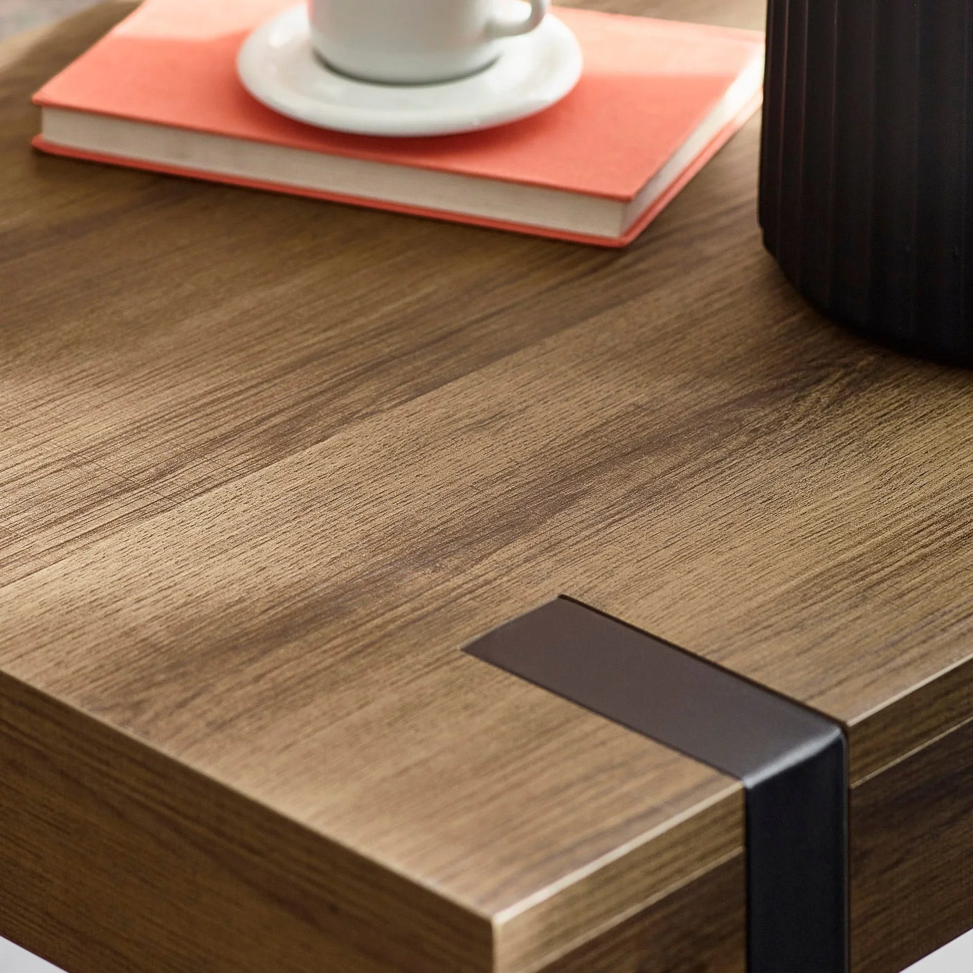 Wooden coffee table corner with black metal detail, book, and cup on top