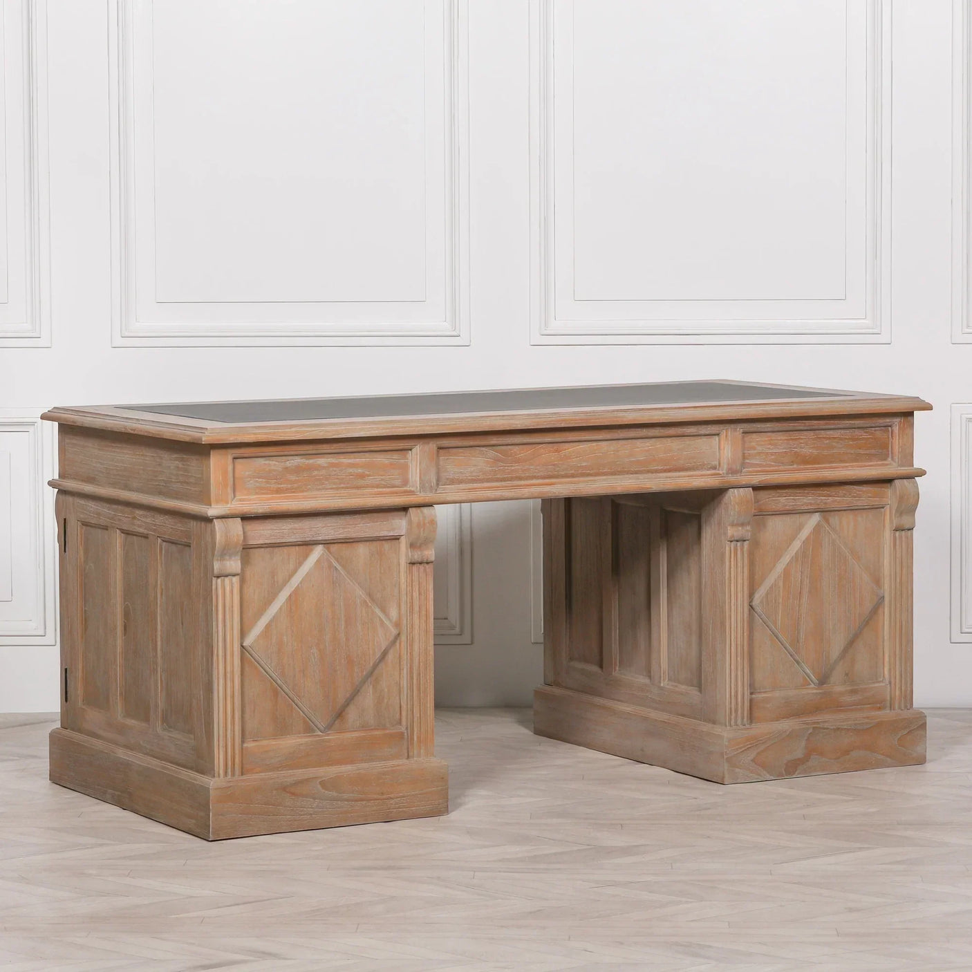 Large wooden desk with carved panel details and black inlay top in bright room