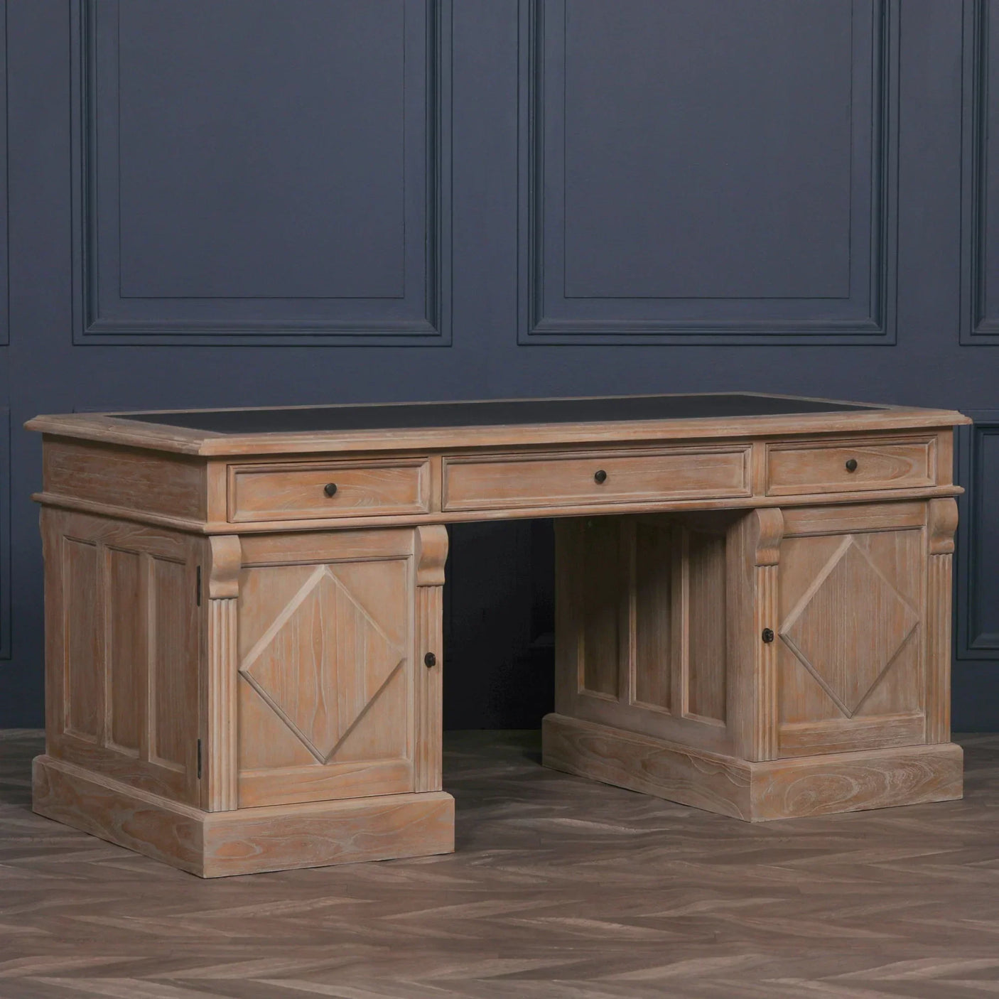 Oak writing desk with three drawers, black top, and paneled sides against dark wall