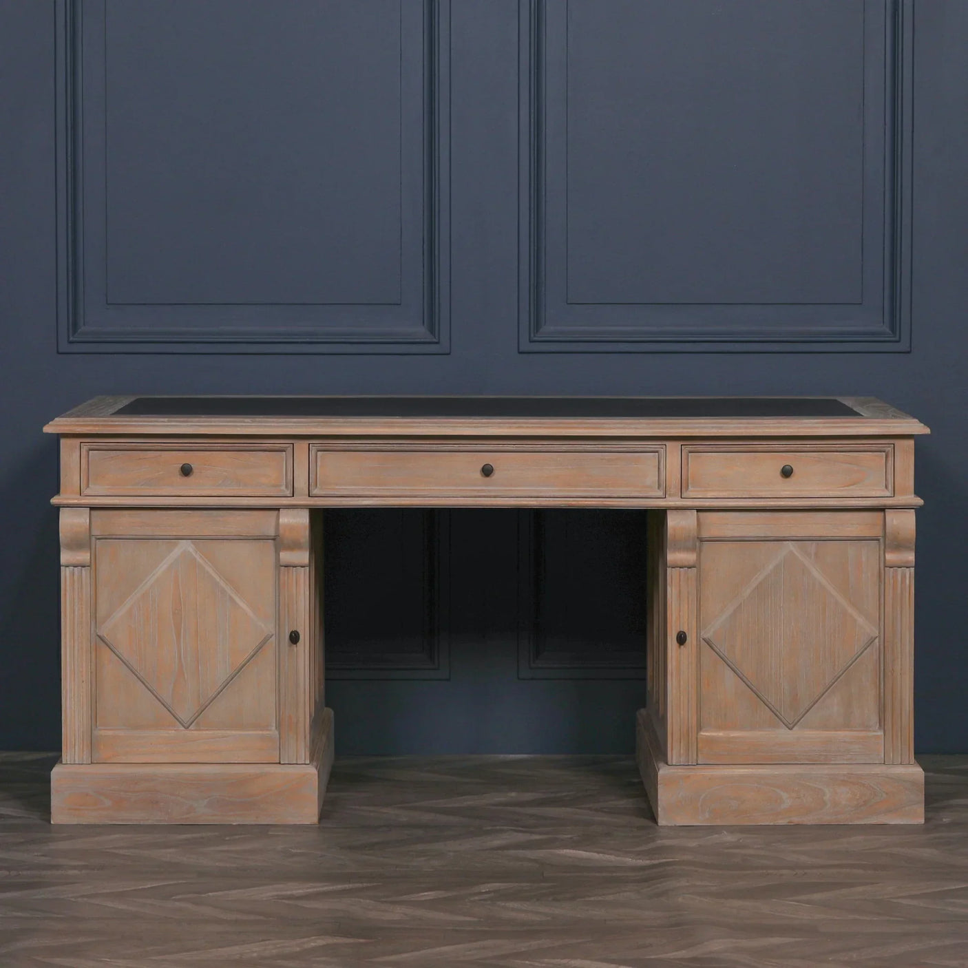 Oak wood office desk with three drawers and panelled cabinet doors against dark wall