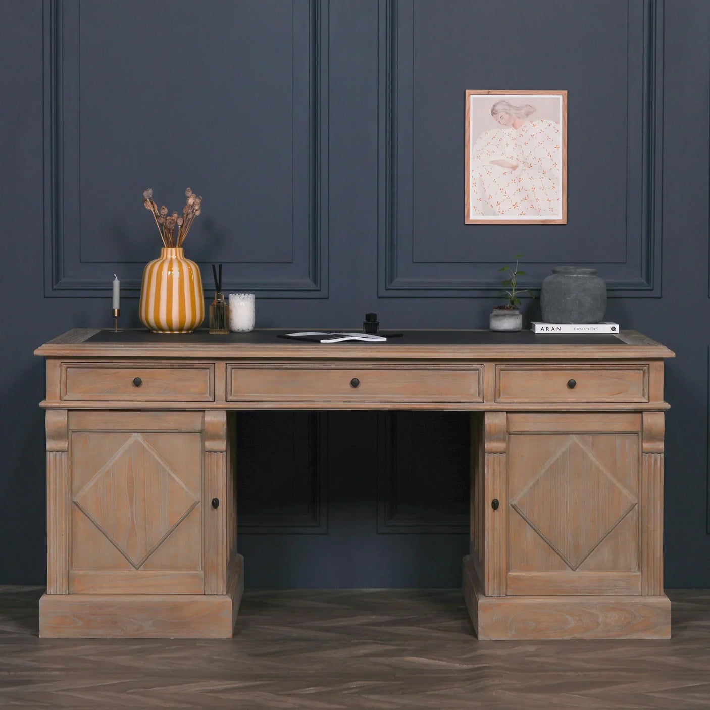 Oak wooden desk with side cabinets and three drawers, styled with vases and books