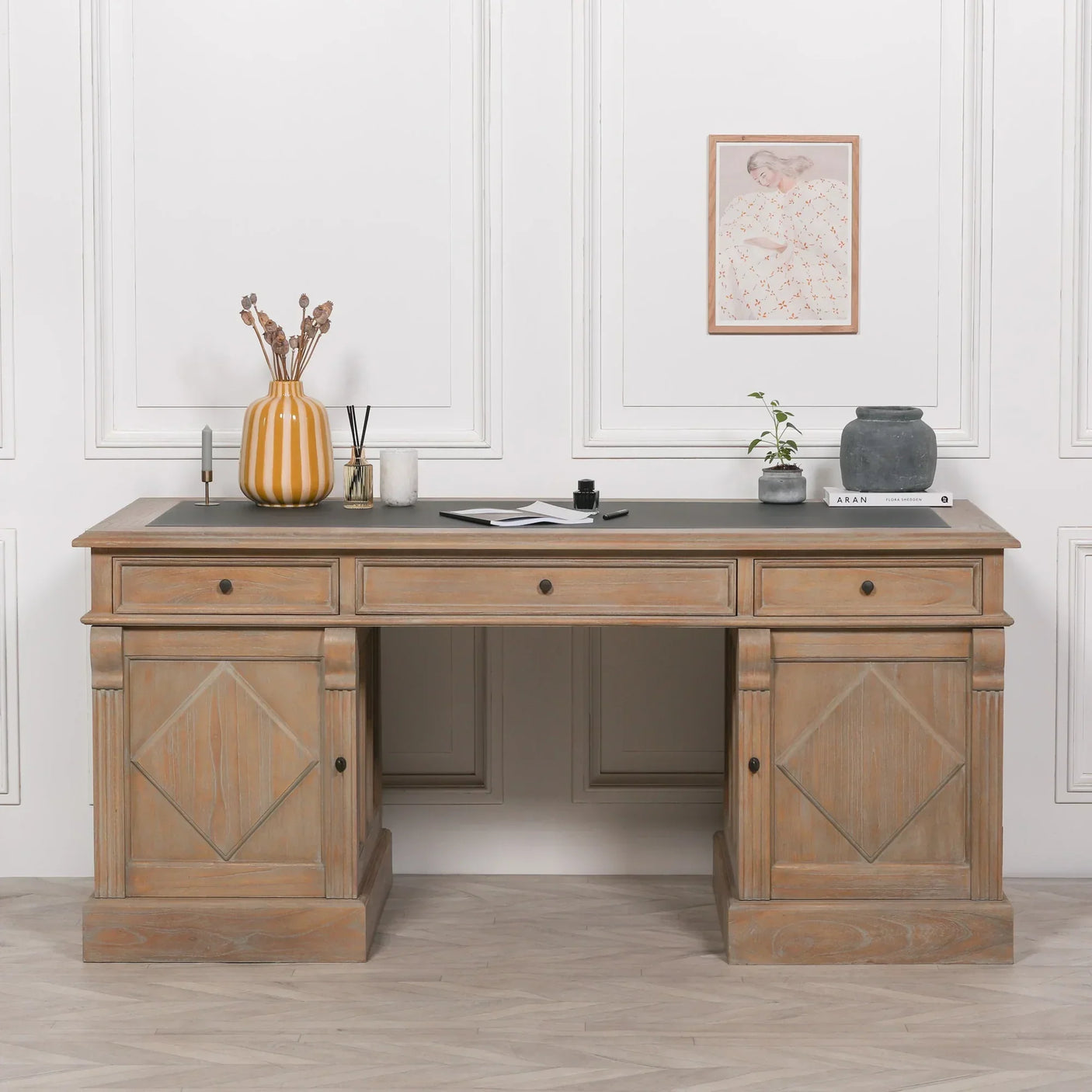 Oak wood office desk with black top and three drawers, styled with vases and decor