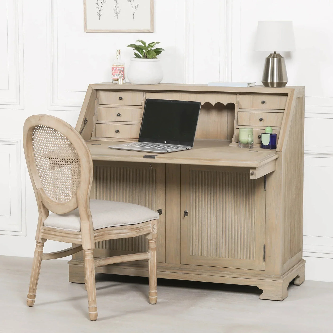 Light wood writing desk with drop-front, storage drawers, laptop, and matching chair