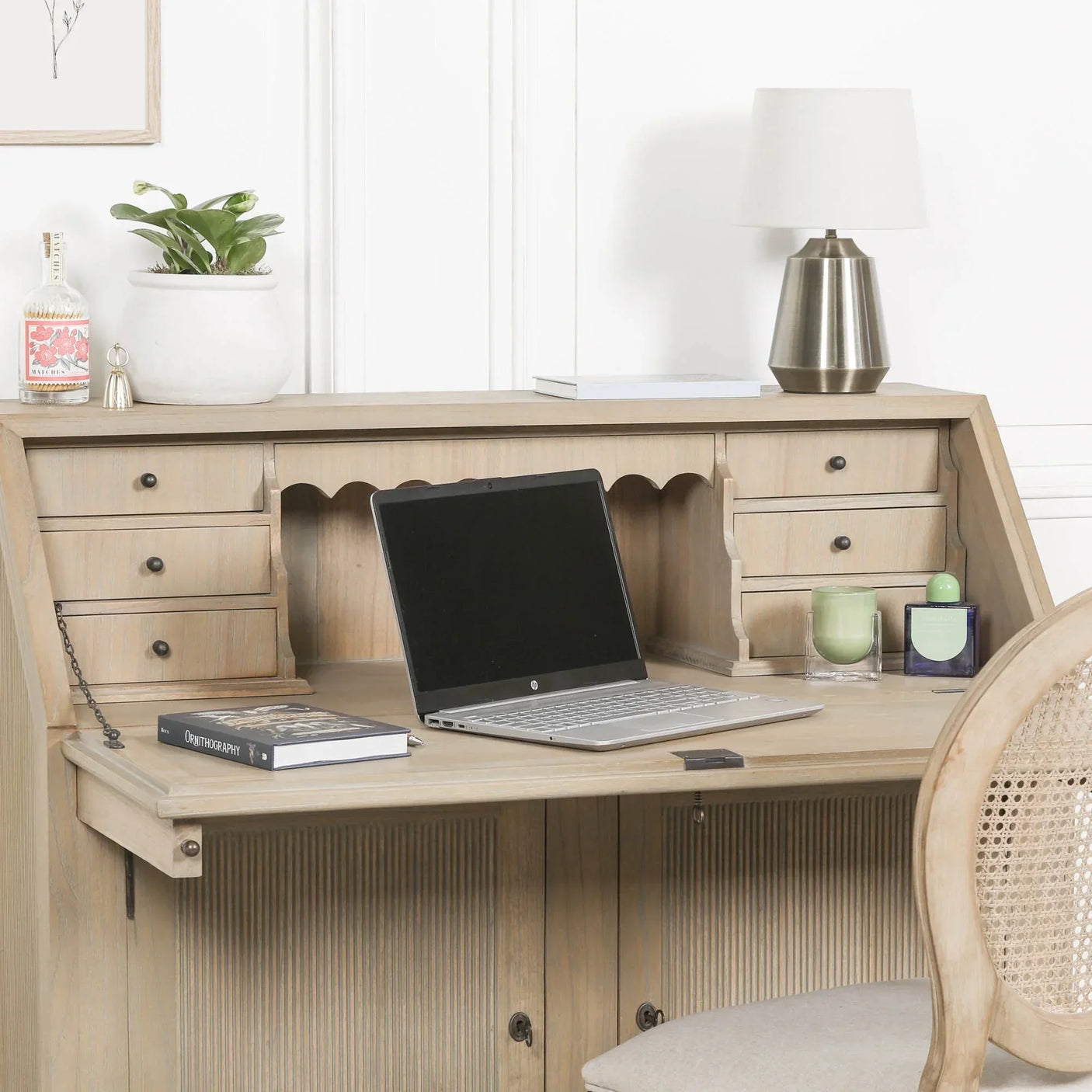 Light wood writing desk with drawers, laptop, lamp, and decorative accessories