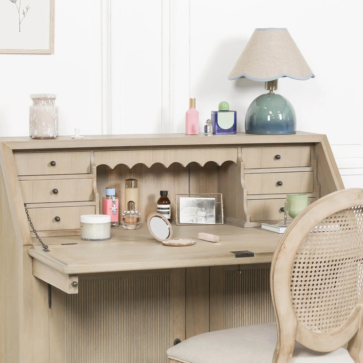 Light oak writing desk with drawers, cane-back chair and vanity items in bright room