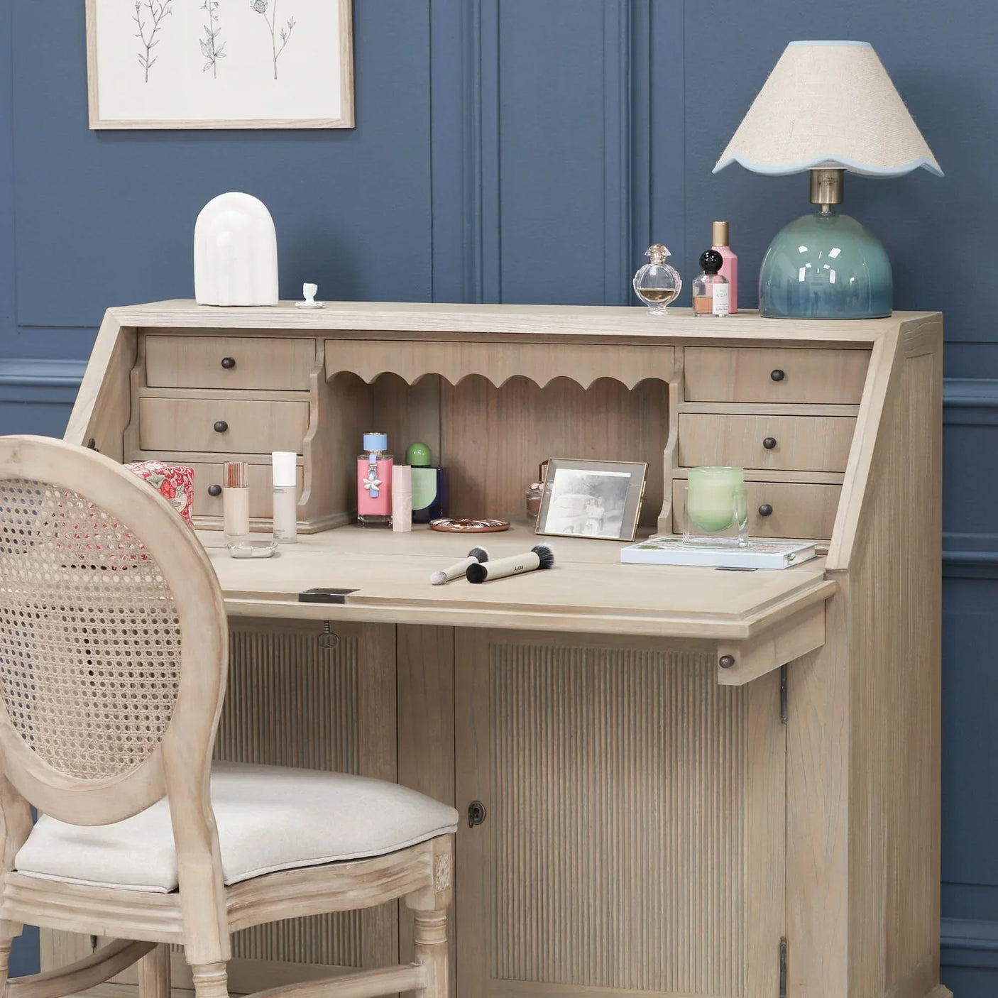 Wooden writing desk with drawers and decor items, cane back chair in front