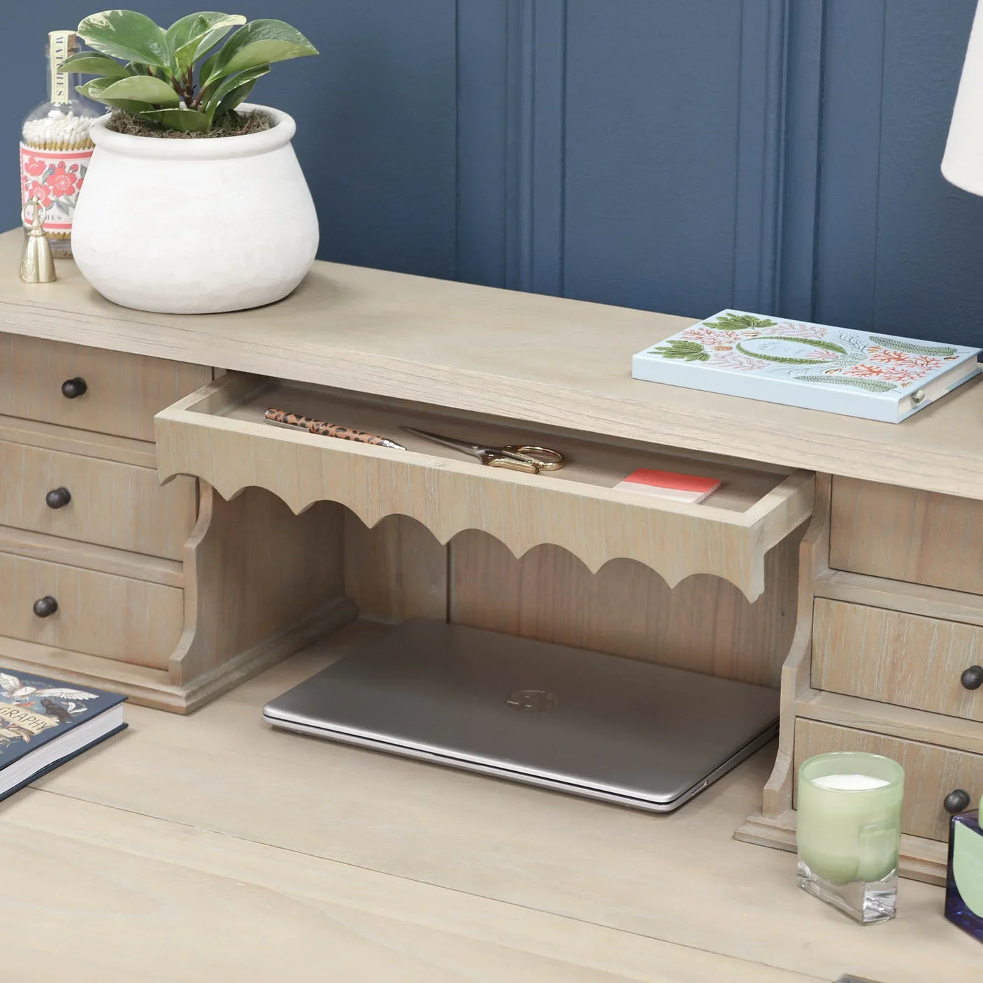 Light wood desk with scalloped drawer, closed laptop and storage drawers