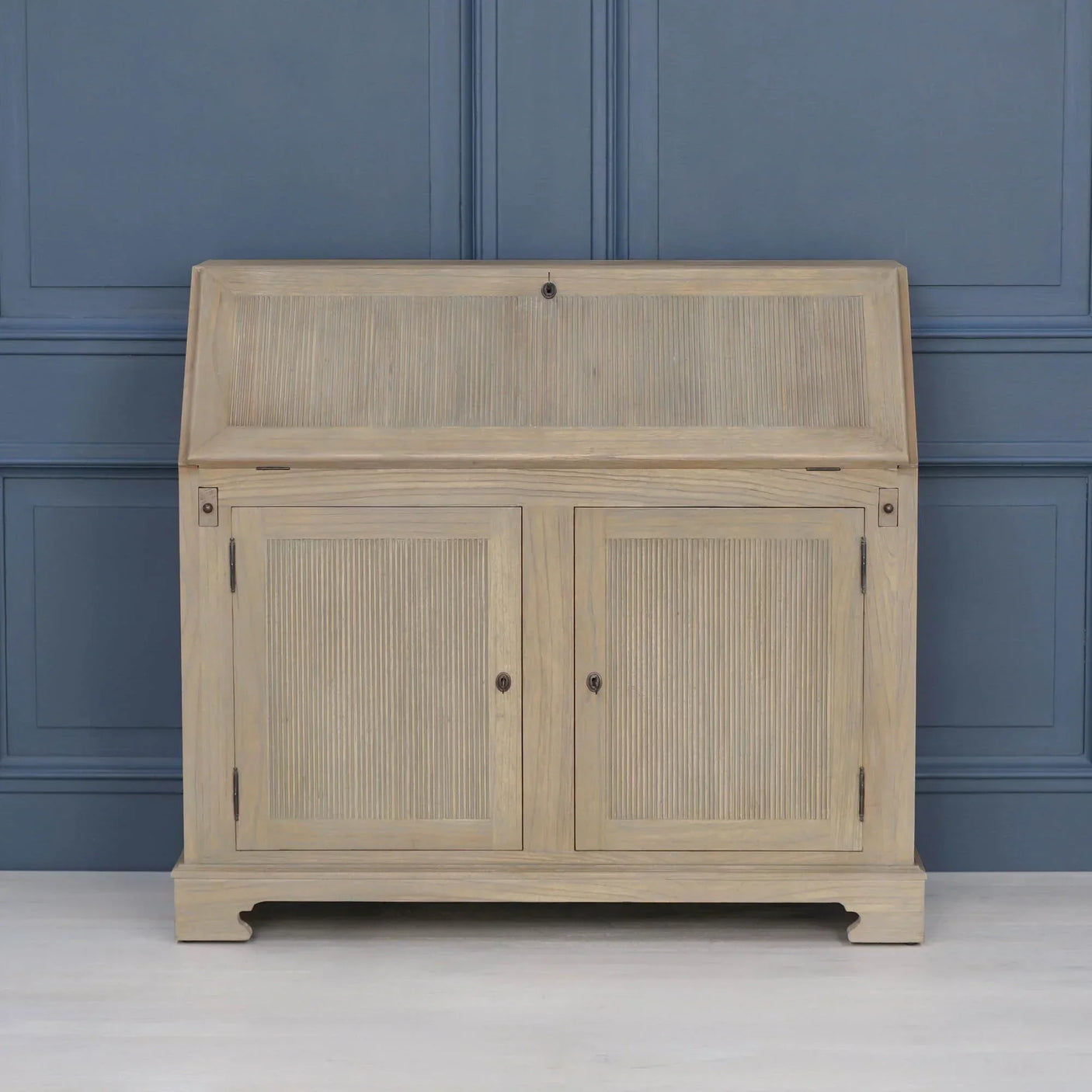 Oak writing bureau with slatted panel doors against blue wall, closed front view