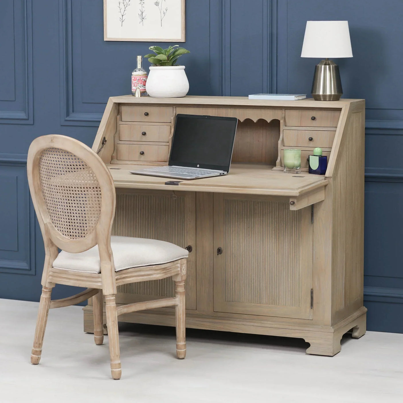 Light wood writing desk with laptop, drawers and upholstered cane chair in home office