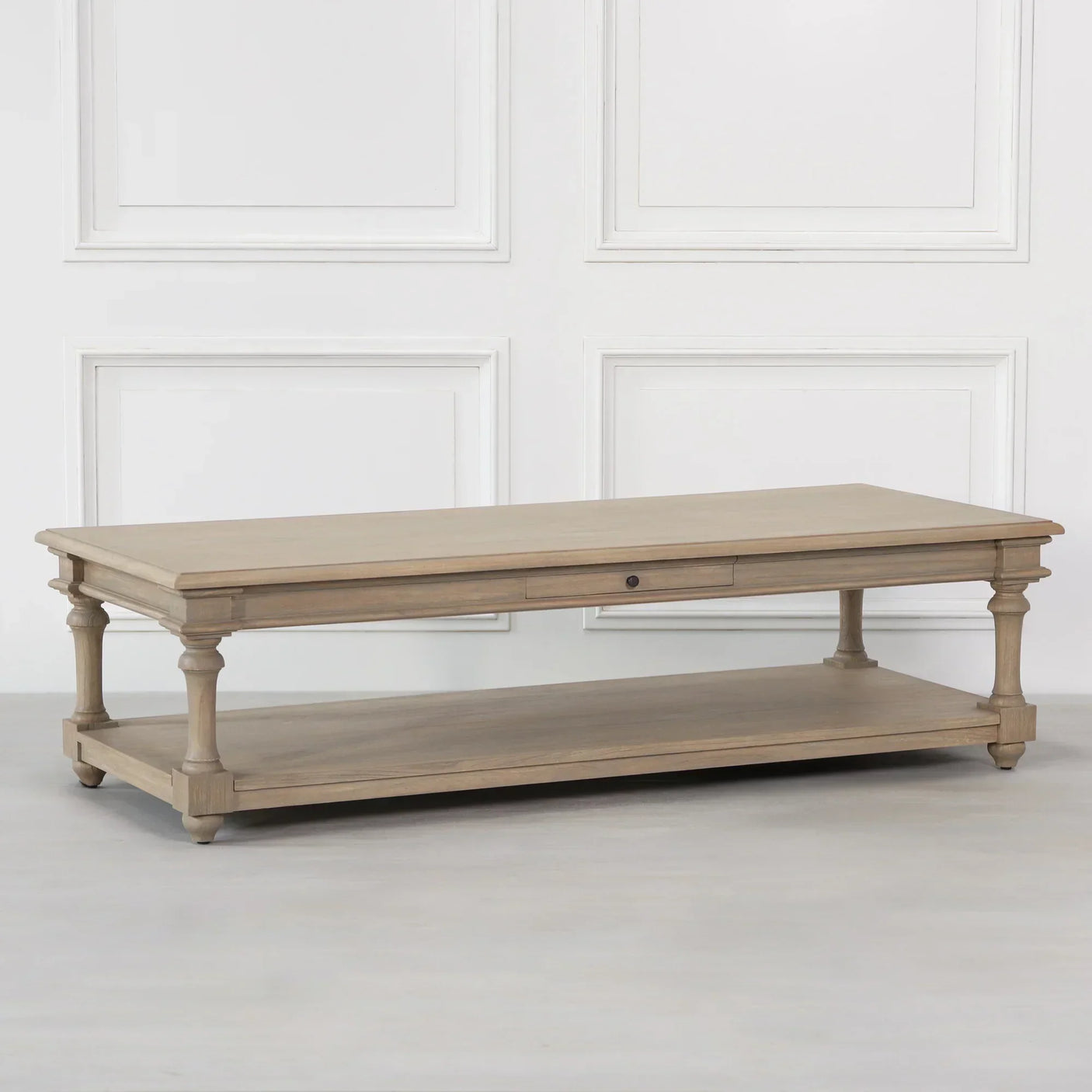 Rustic wood coffee table with turned legs, drawer, and lower shelf in light oak finish