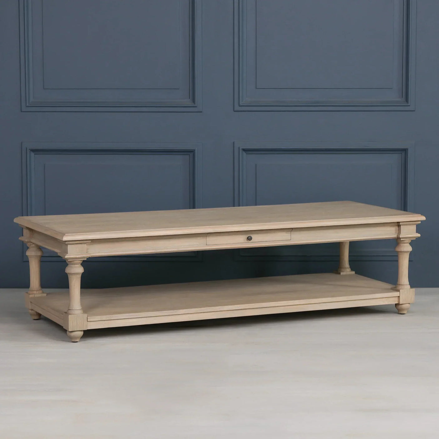 Light wood coffee table with lower shelf and single drawer against blue panel wall
