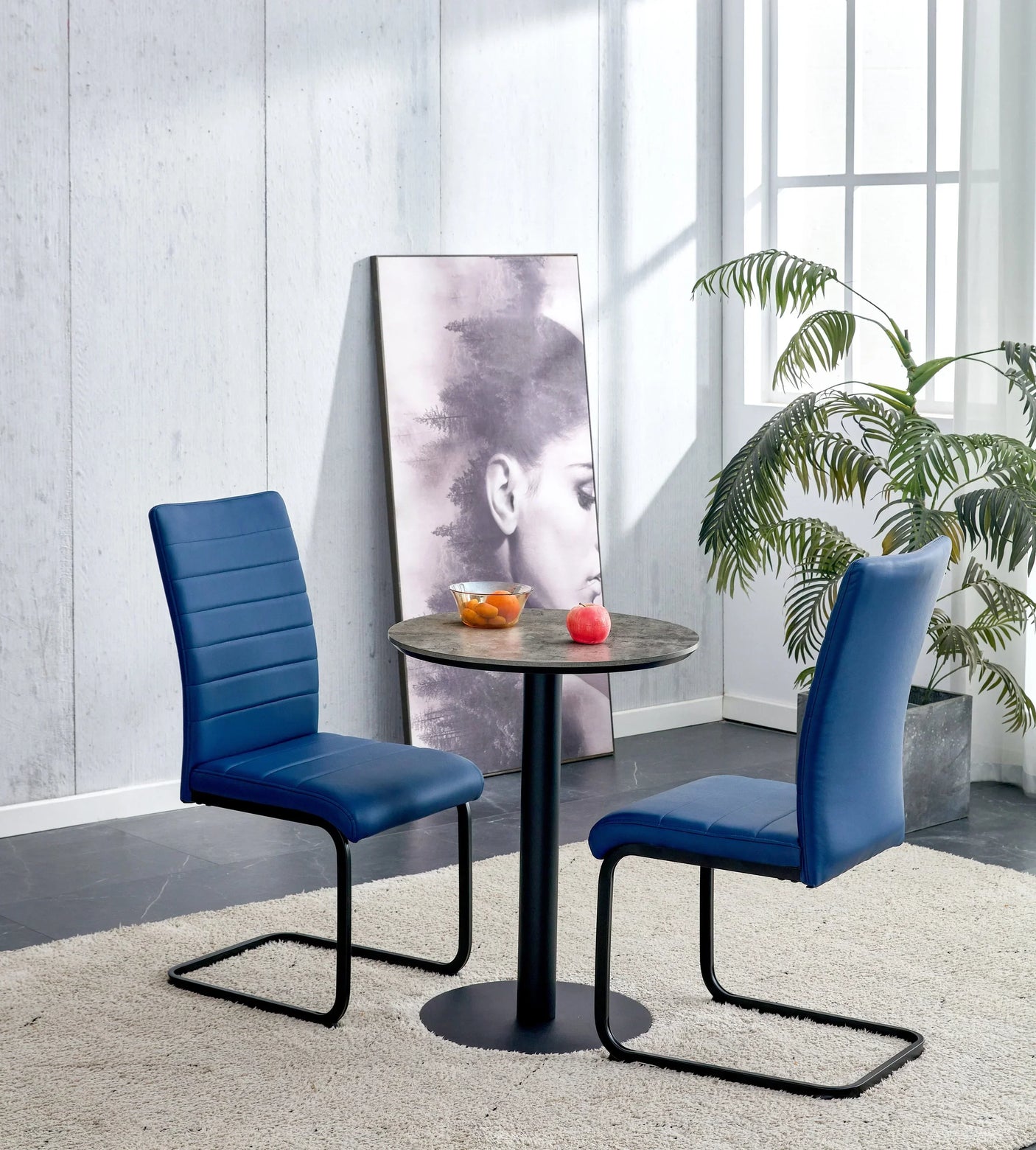 Round grey dining table with black legs and two blue dining chairs on cream rug