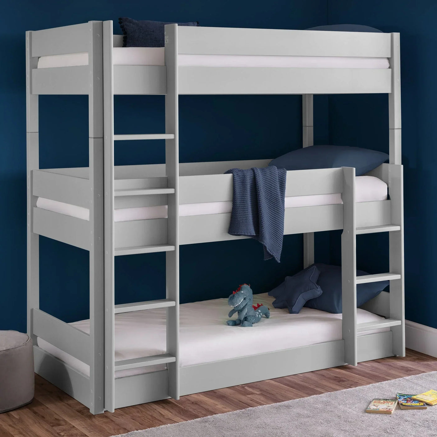 Grey wooden triple bunk bed with ladders in a kids bedroom, blue walls, hardwood floor