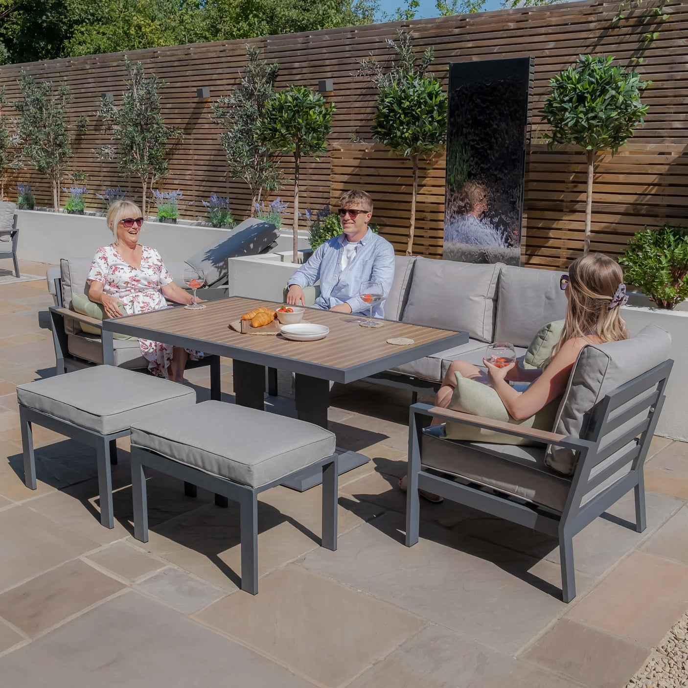 Grey outdoor garden sofa set with dining table, benches, and people relaxing on a patio