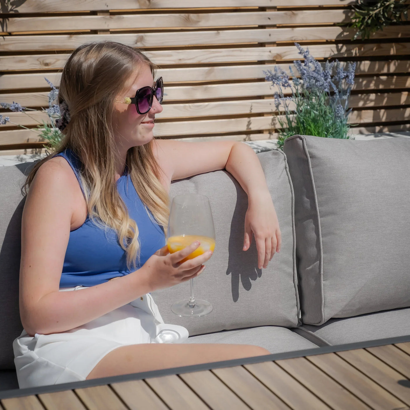 Grey outdoor sofa with cushions and woman relaxing in garden setting