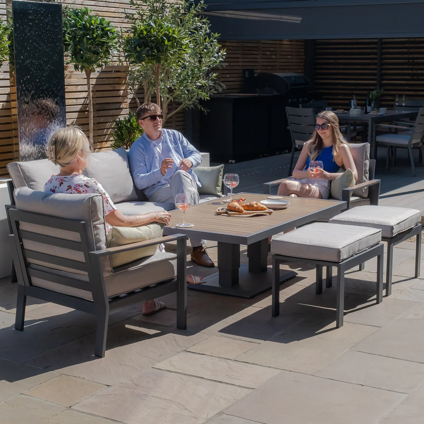 Grey outdoor garden furniture set with cushions and dining table on patio, people relaxing