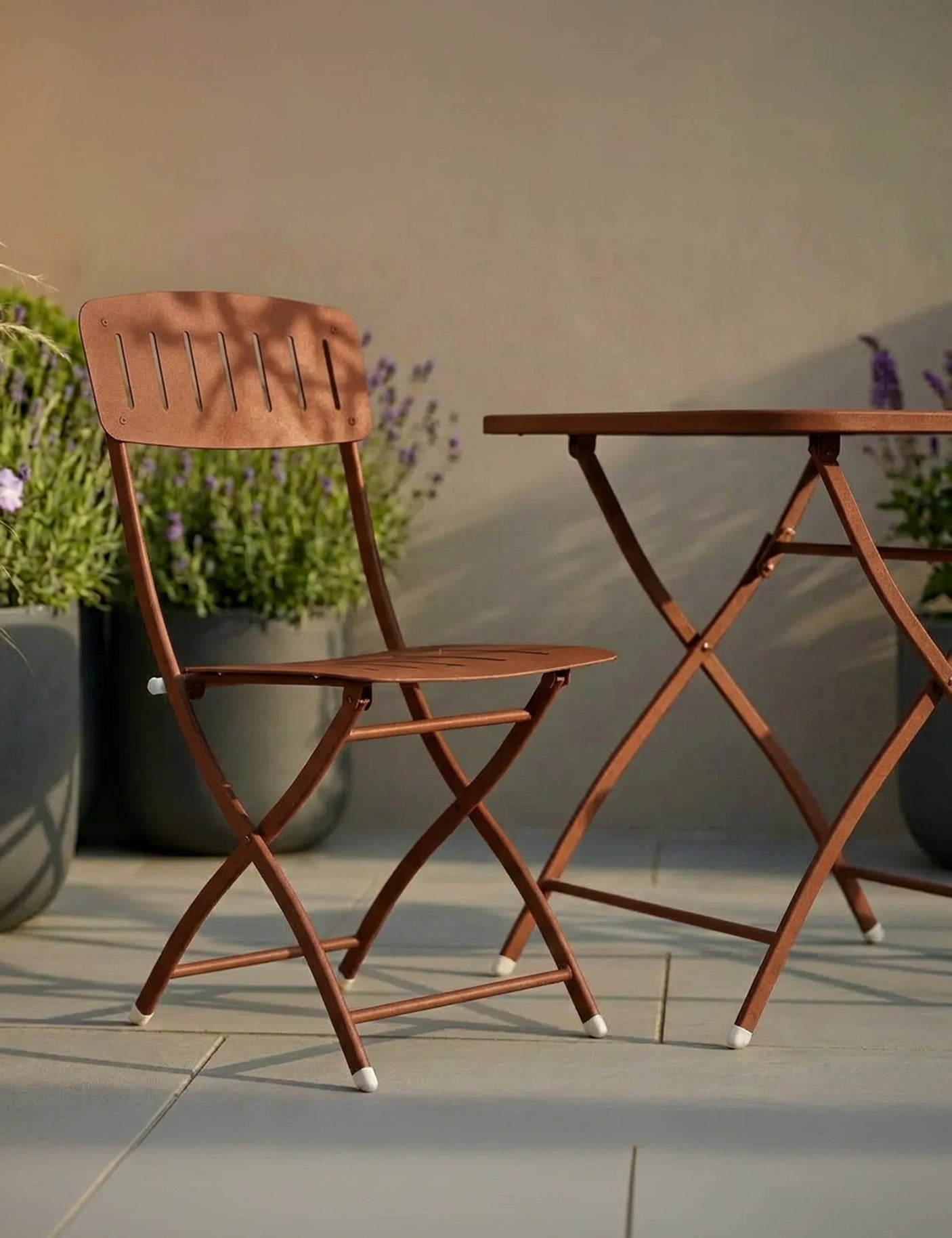 Brown folding garden chair and table set on patio with potted plants in background