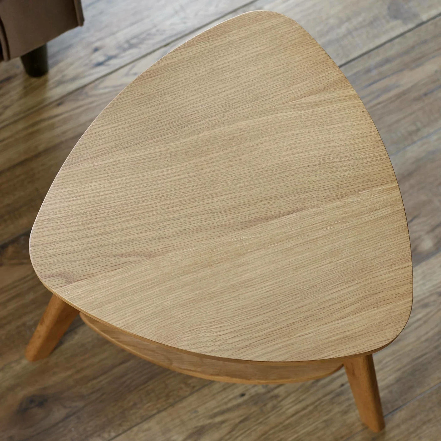Light oak coffee table with rounded triangular top on wood floor, angled overhead view