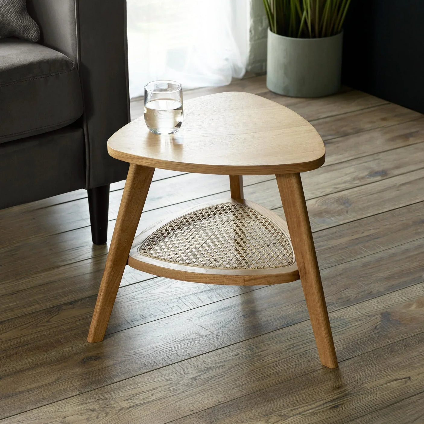 Oak side table with rounded triangular top and lower rattan shelf in living room setting