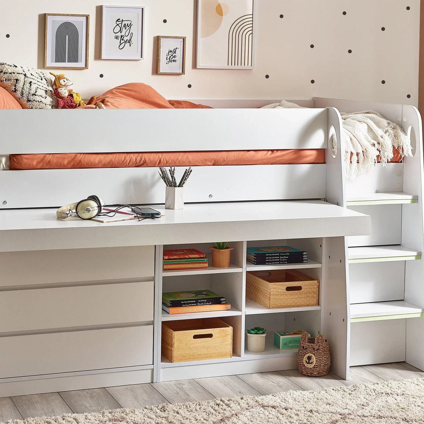 White midsleeper bed with desk, drawers and shelving, orange bedding, and wall art accents
