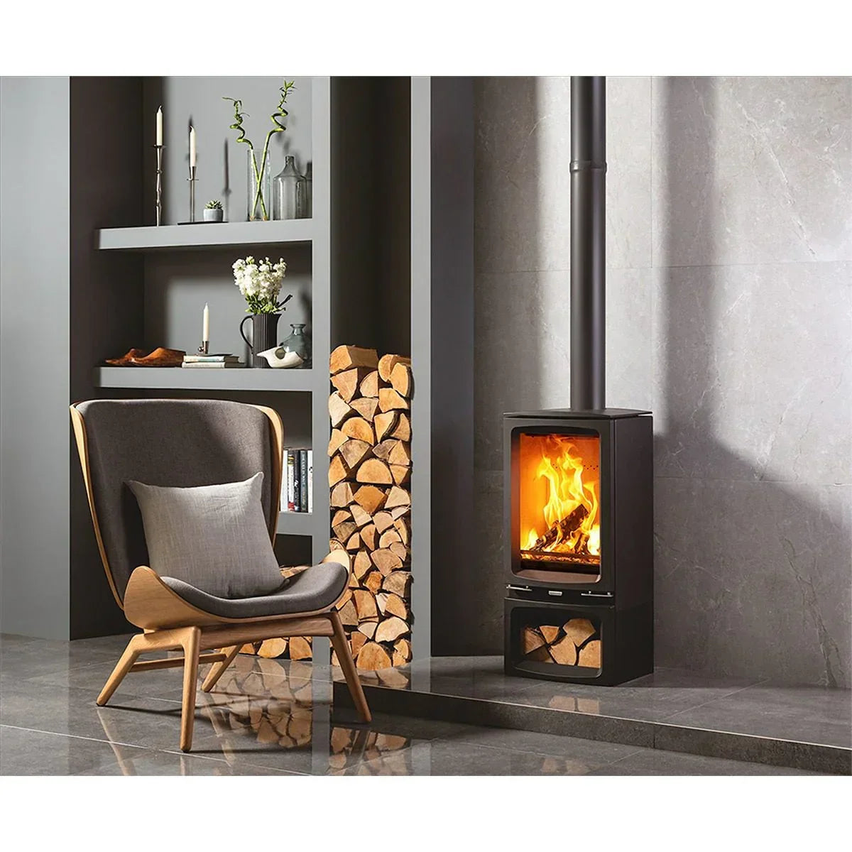 Modern wood burning stove with stacked logs beside grey lounge chair and shelves