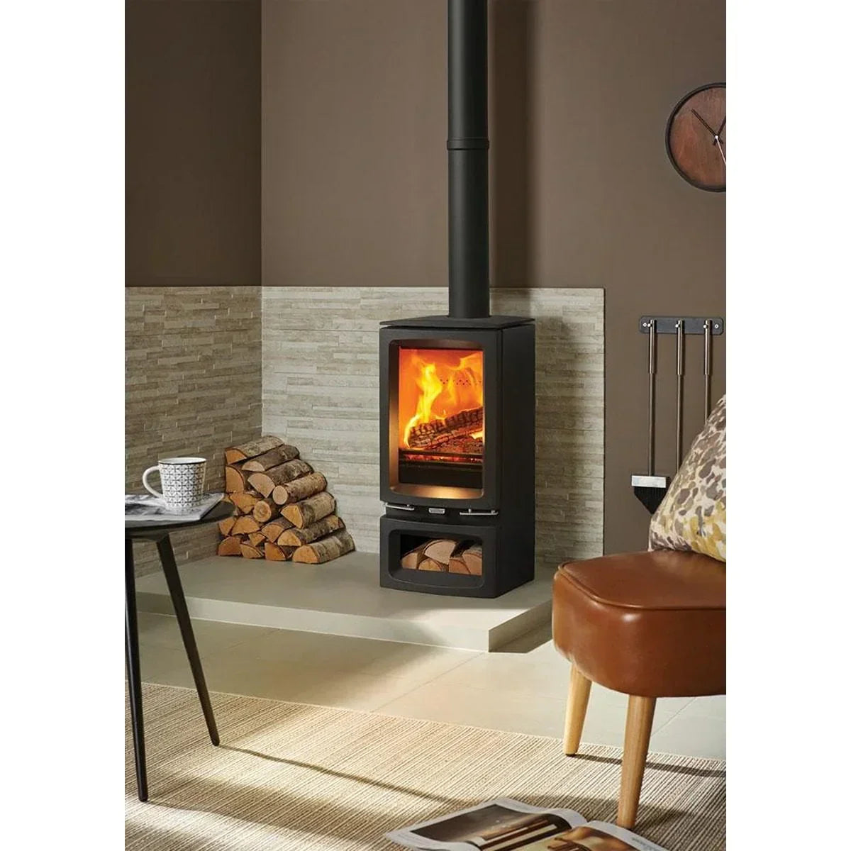 Modern wood burning stove with visible fire, stacked logs, tools, and seating area