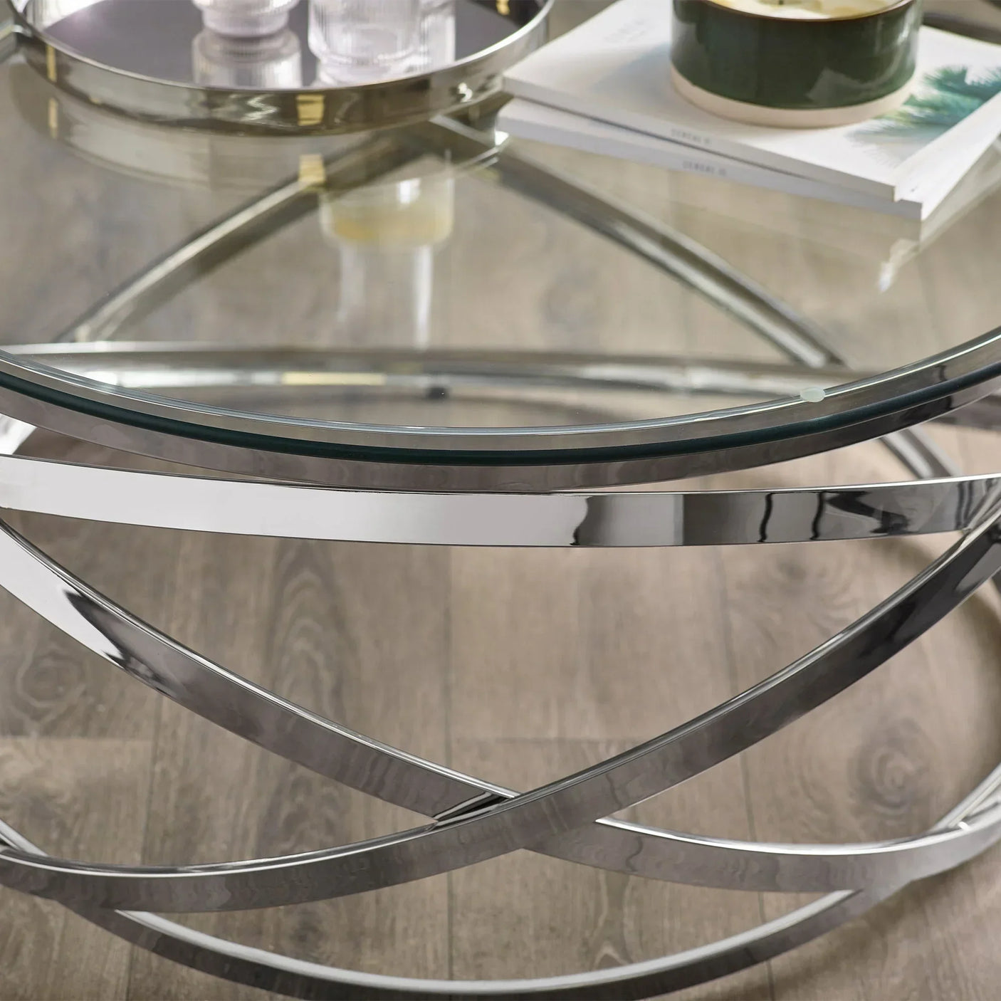 Glass coffee table with chrome metal base and books on wood floor