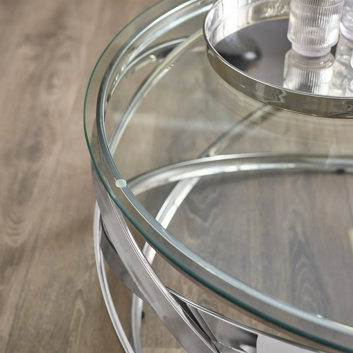 Round glass coffee table with chrome metal base and tray on wooden floor