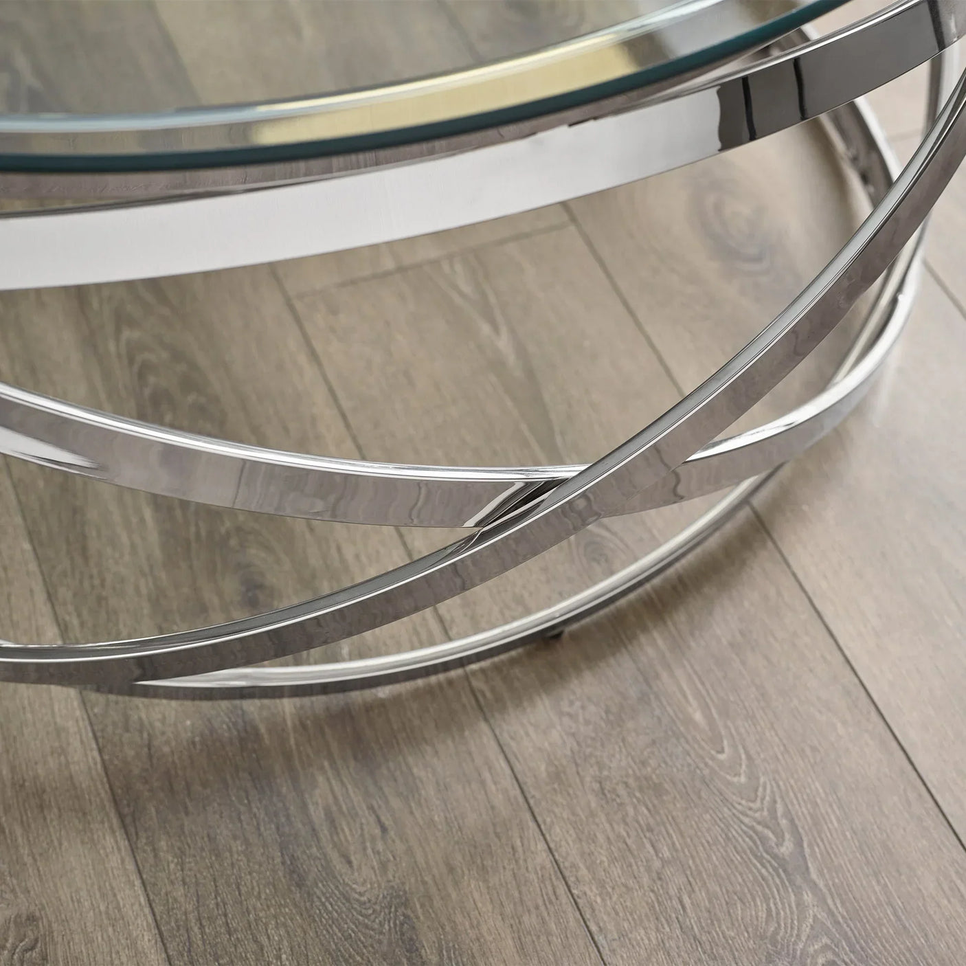 Round glass coffee table with chrome metal frame on wood floor, close-up of base