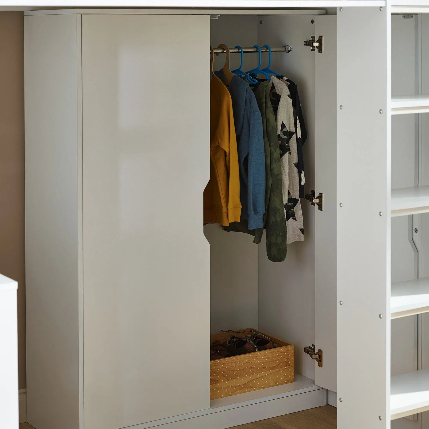 White wardrobe with hanging rail, kids’ clothes on hangers, and wooden storage box