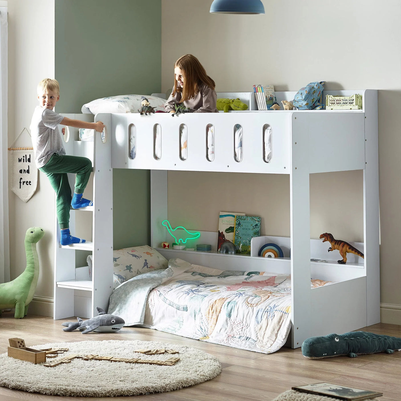 white wooden bunk bed with ladder in kids bedroom, dinosaur decor, books and toys visible