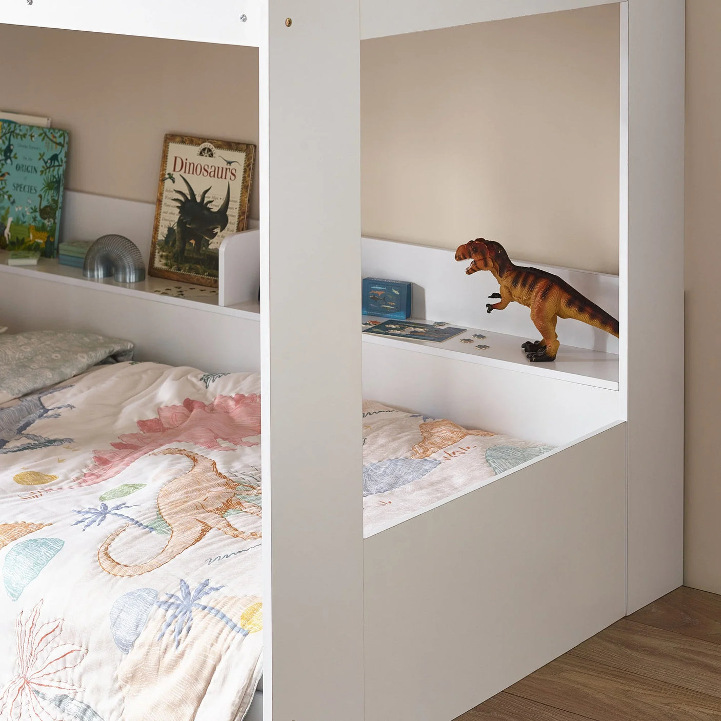 White children's bed with dinosaur bedding, bookshelf headboard, and toy dinosaur figure