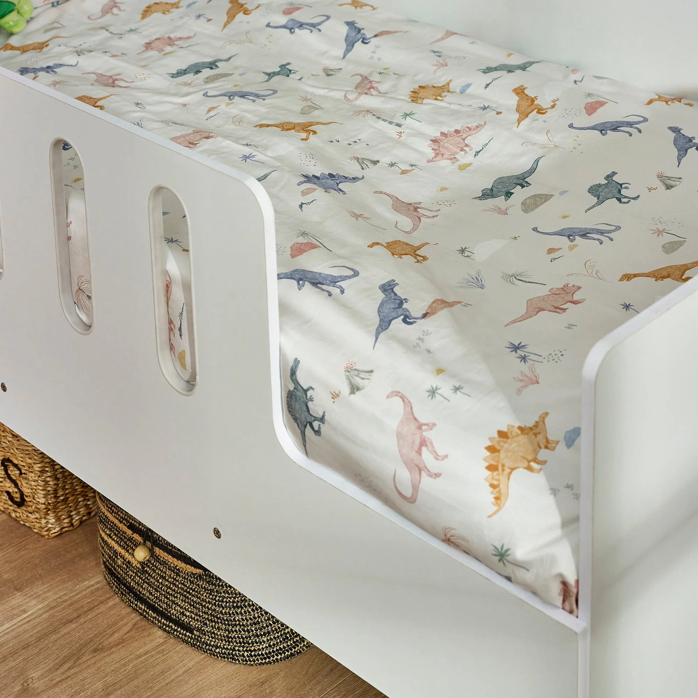 White toddler bed with colorful dinosaur print bedding and built-in guard rail