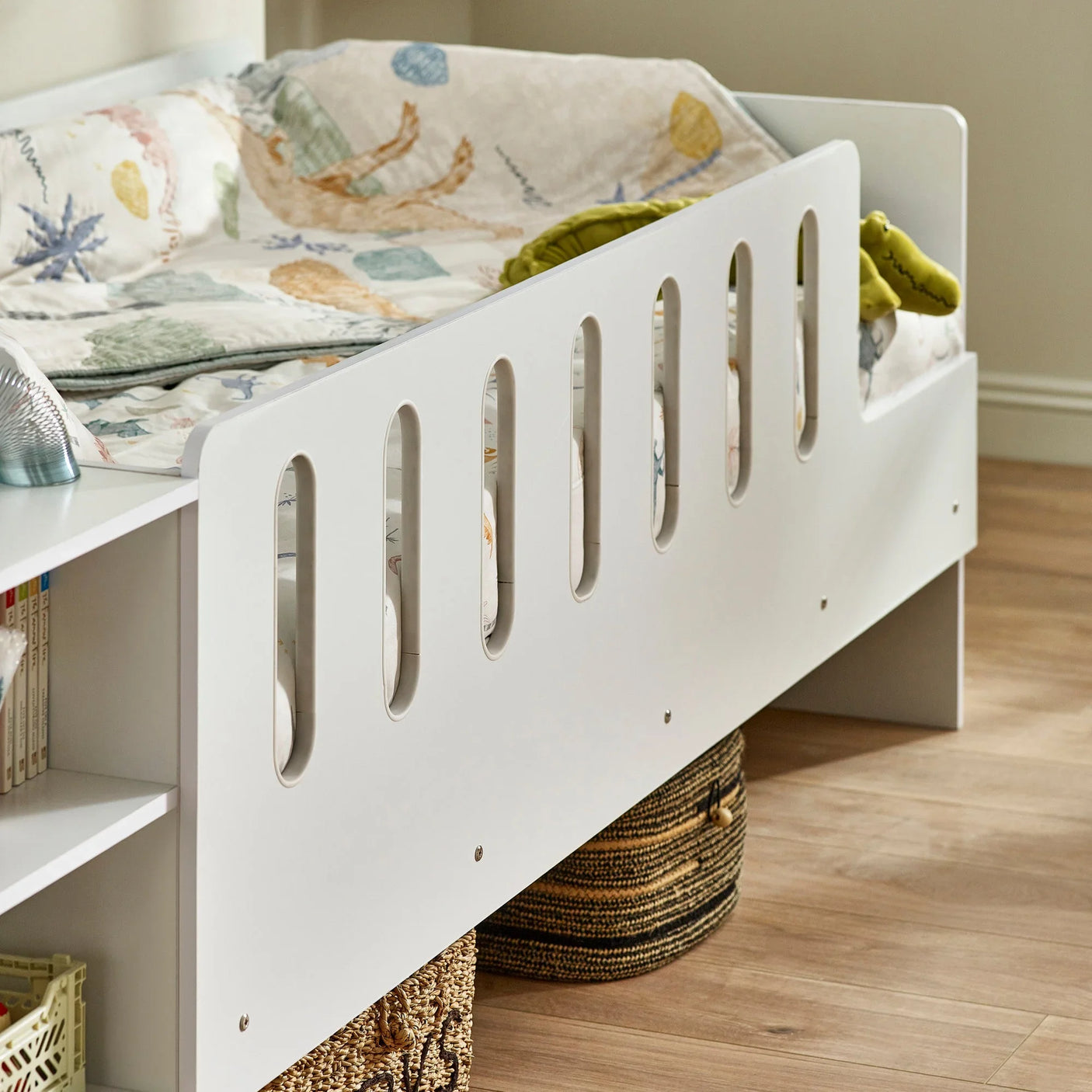 White kids bed with side guard, patterned bedding, bookshelf and storage baskets underneath