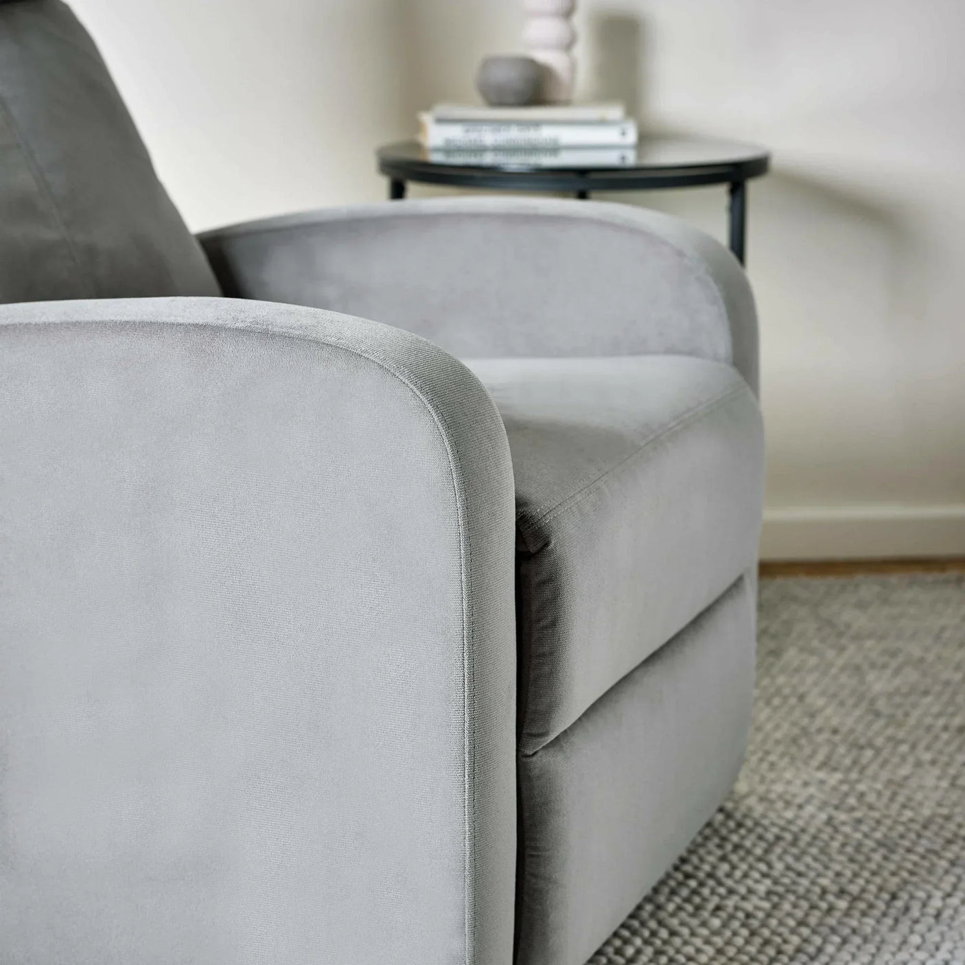 Grey fabric armchair with rounded armrest on textured rug near side table