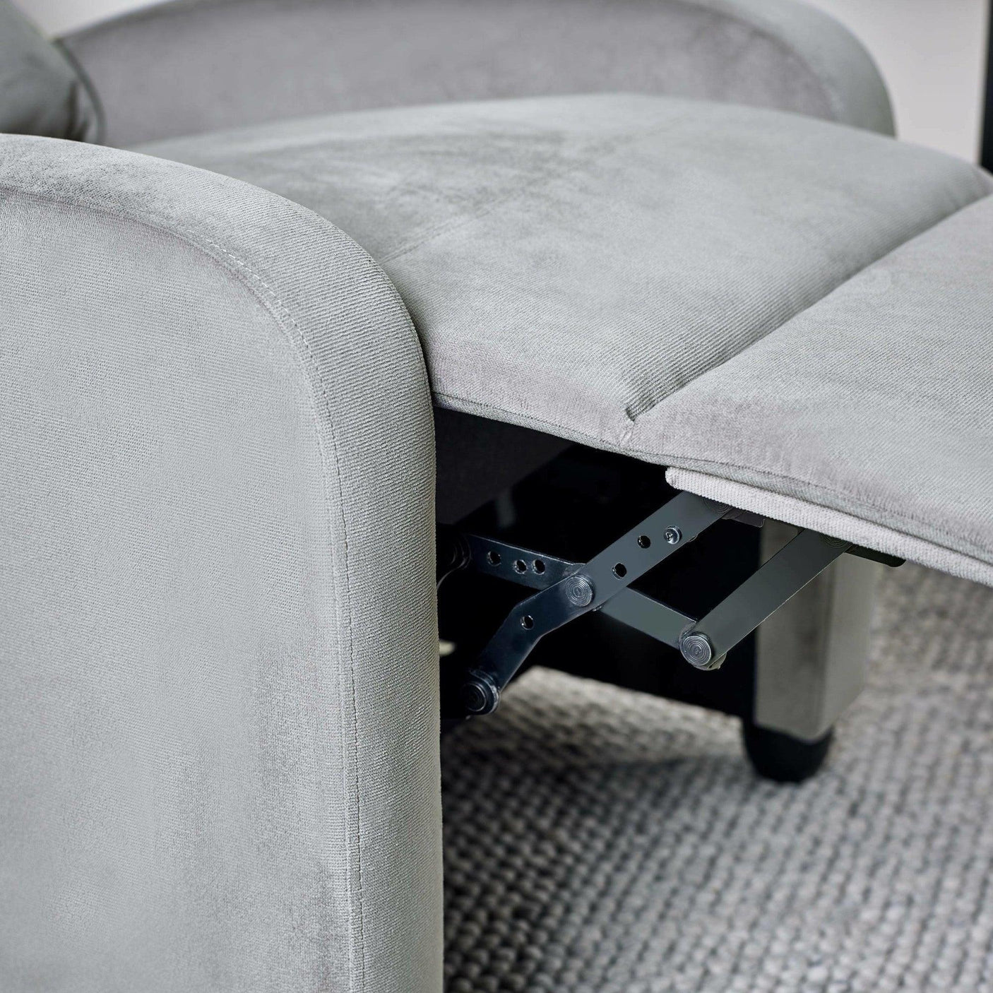 Closeup of grey fabric recliner chair footrest and metal mechanism on textured rug