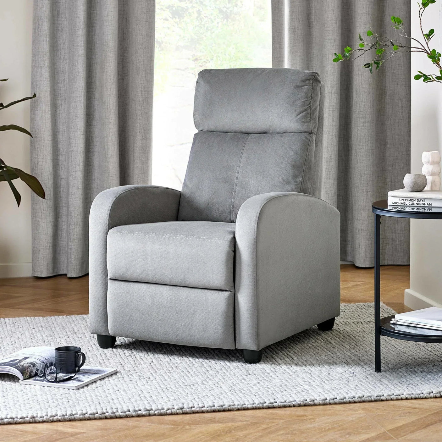 Grey fabric recliner chair on rug in modern living room with coffee table and plant