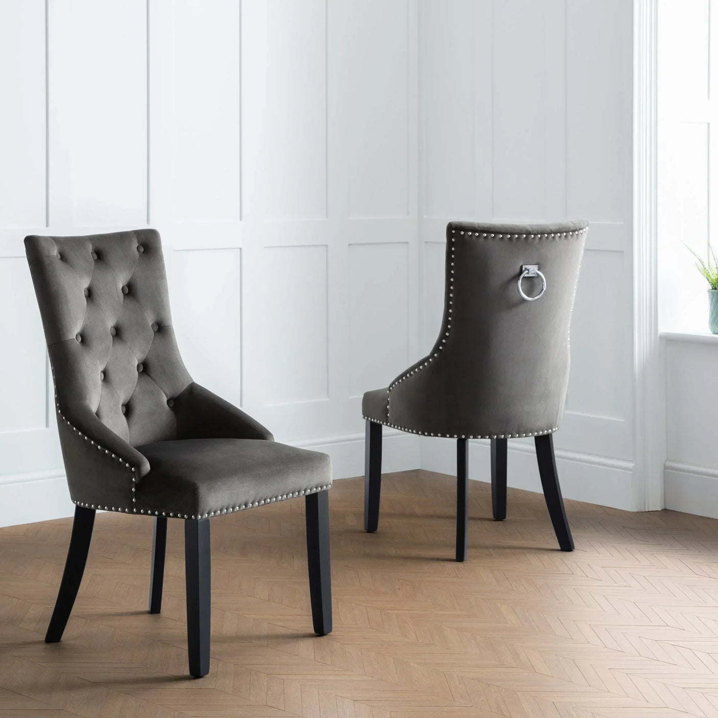 Grey velvet knockerback dining chairs with button detail and stud trim on wood floor