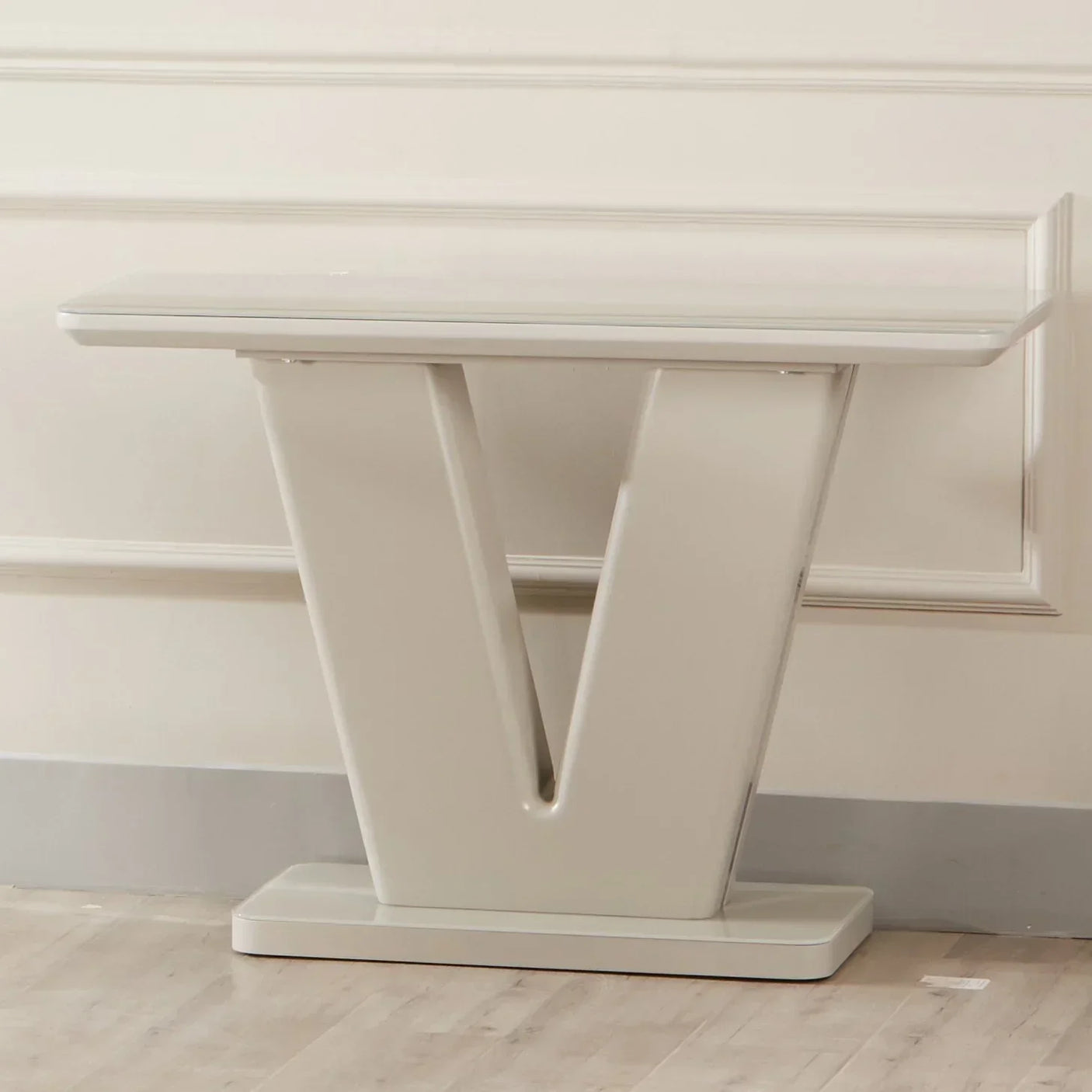 Cream console table with V-shaped base against wall on light wood floor