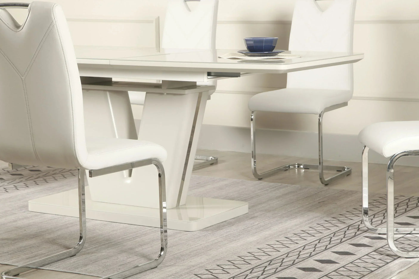 White extension dining table with chrome legs and matching chairs on patterned rug