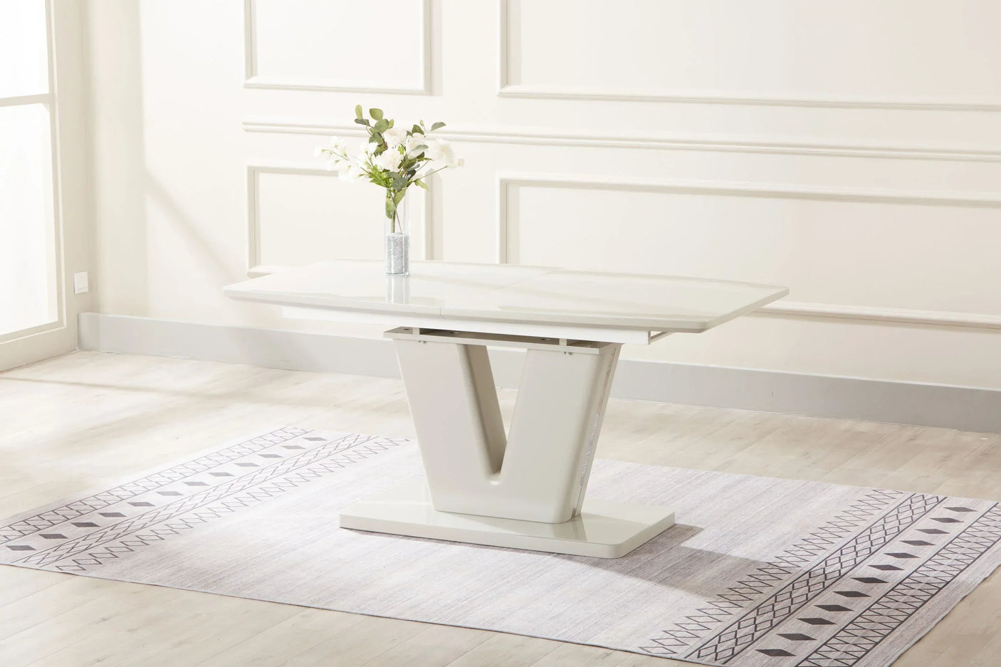 Glossy white extension dining table with V-shaped base on patterned rug in modern room
